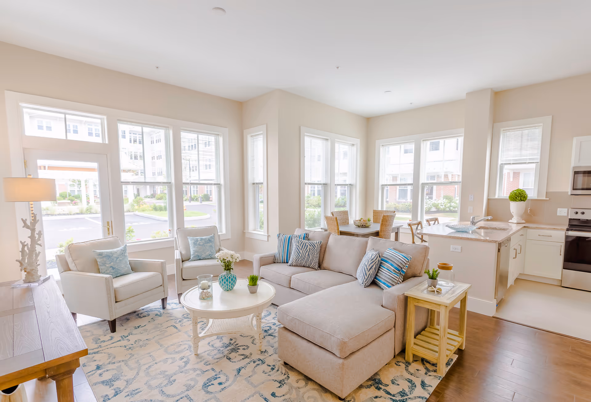 Bright, airy open-concept living room and kitchen with a beige sectional sofa, armchairs, round coffee table, dining nook, and large windows.