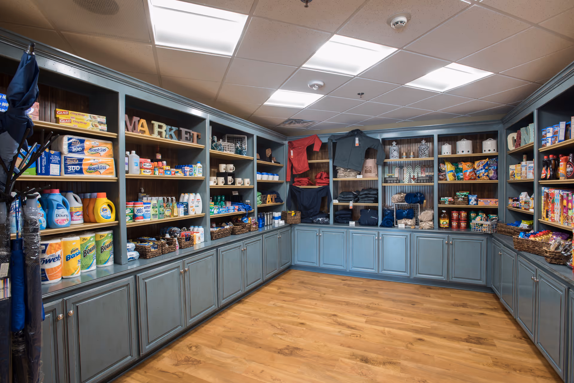 Small on-site market inside a senior living facility with shelves stocked with household supplies, snacks, and clothing.