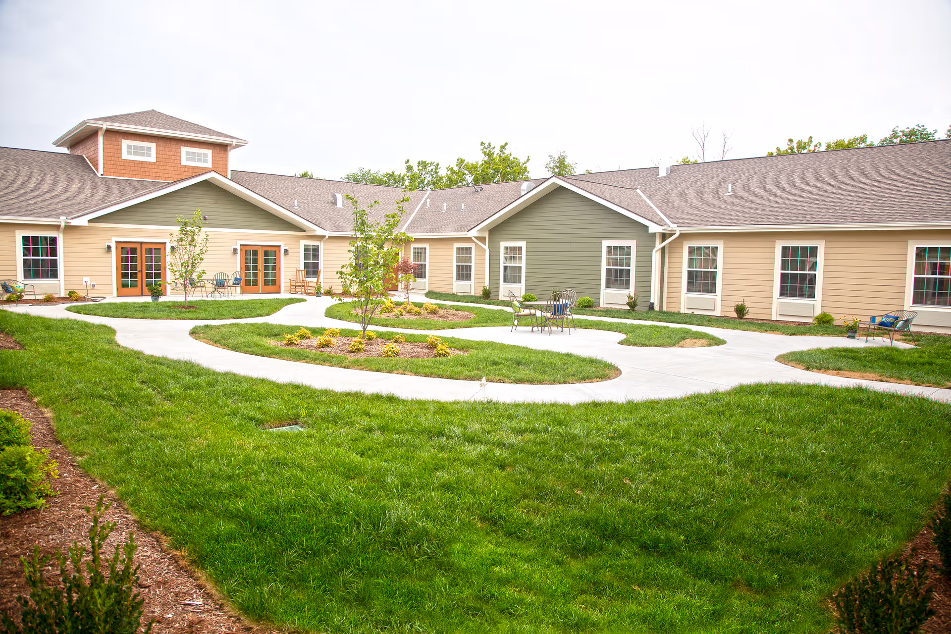 Well-maintained courtyard with winding concrete paths, patio chairs, small landscaped islands, and a surrounding single-story building.
