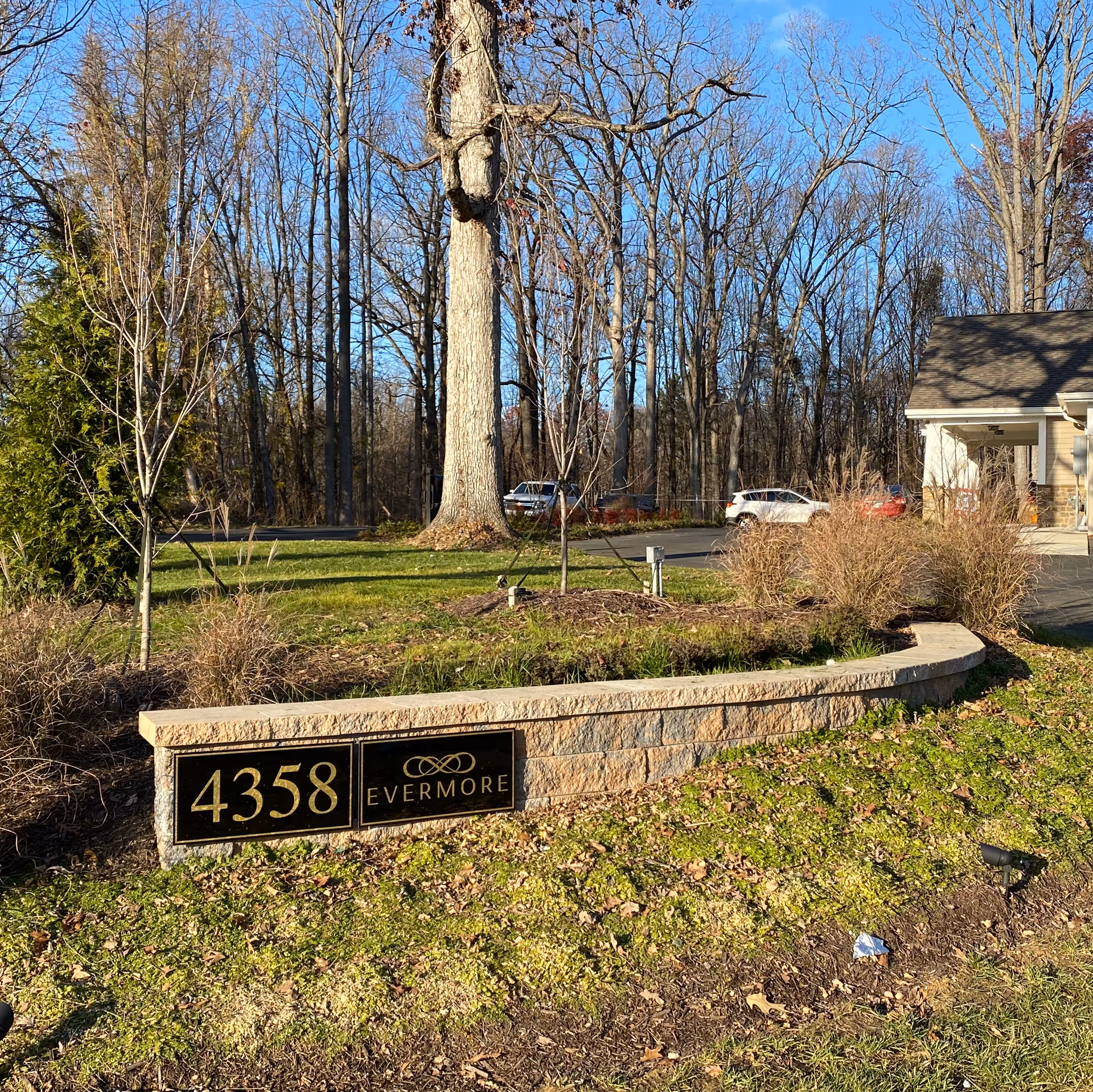 Stone entrance sign displaying "4358" and "Evermore" on a landscaped lawn with trees and part of the building in the background.