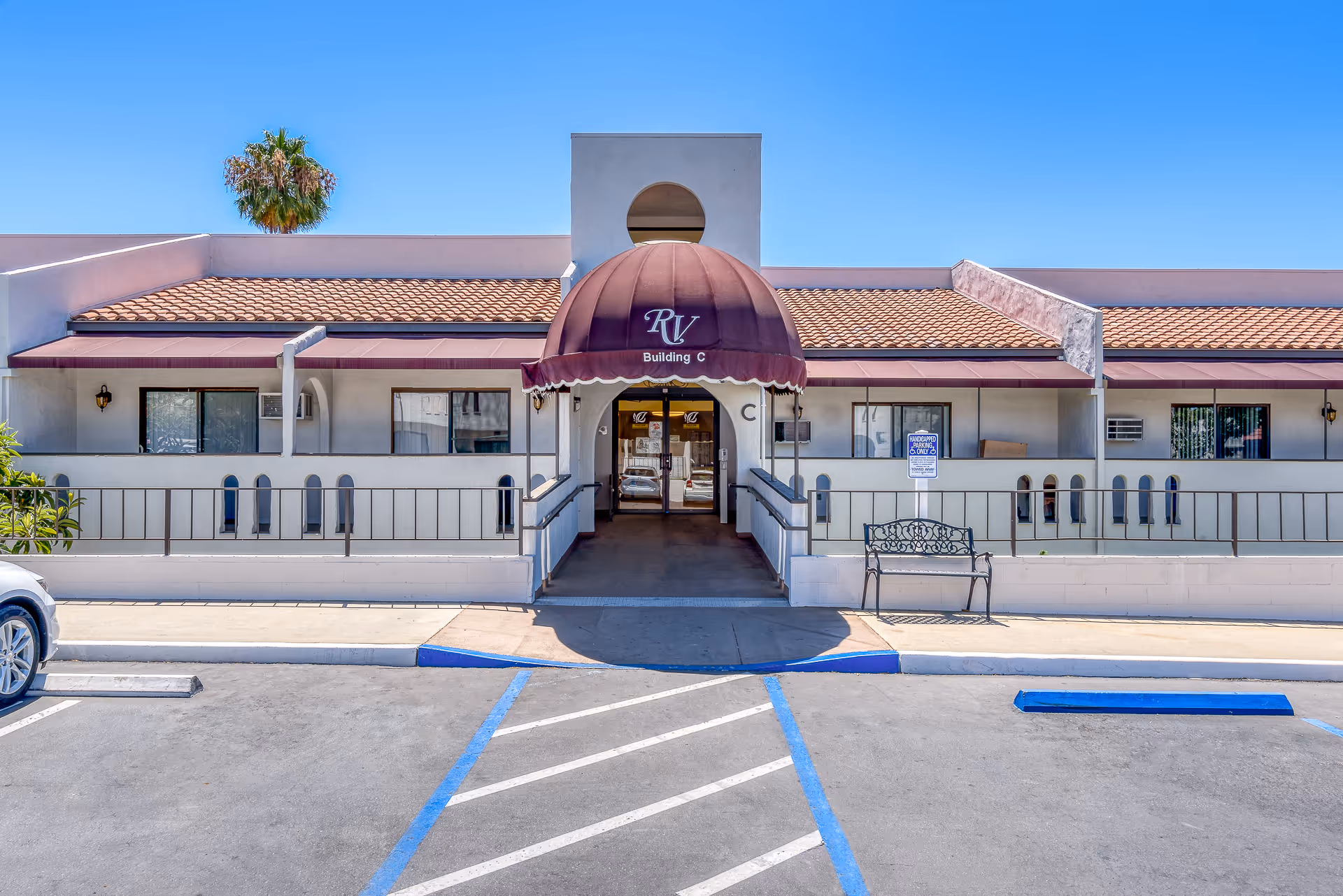 Front entrance of Rancho Vista Senior Living Building C with a maroon canopy, ramped walkway, and parking spaces in front.