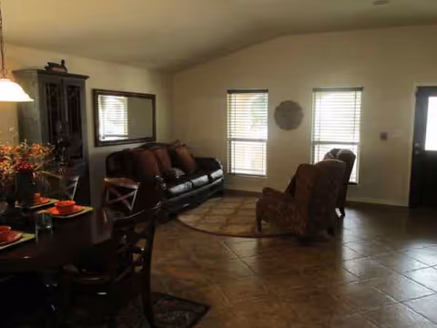 Cozy living room with sofa, chairs, dining table, and windows in a senior living facility.