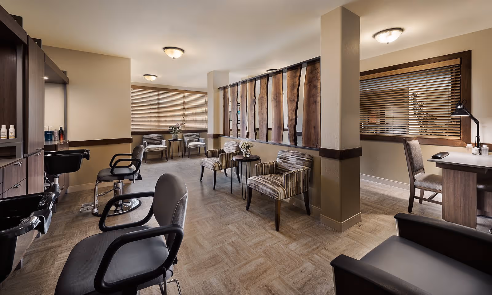 Interior salon and lounge area with styling chairs, shampoo sinks, striped lounge chairs, and a reception desk.