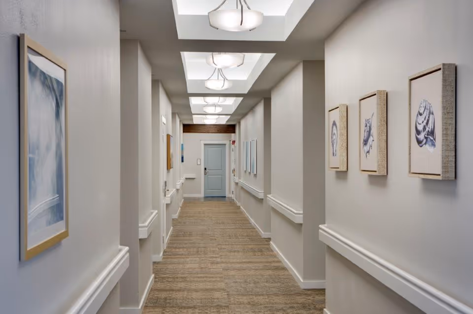 Well-lit interior hallway with handrails, framed artwork on the walls, recessed ceiling lights, and a door at the far end.