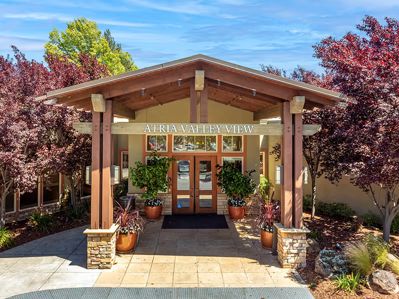Entrance of Atria Valley View with wooden portico, potted plants, and surrounding trees.