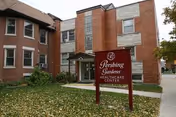Exterior view of a brick senior care building with a front entrance and sign.