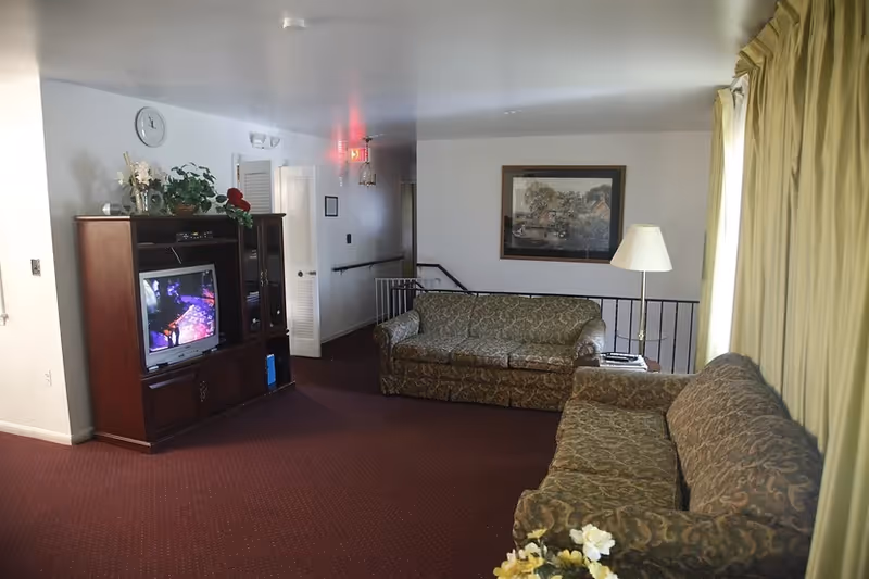 Cozy senior living room with patterned sofas, a TV cabinet, and curtains.