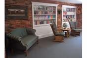 Cozy sitting area with built-in bookshelves against a brick wall, two wooden rocking chairs, a small round table, and a cushioned loveseat.