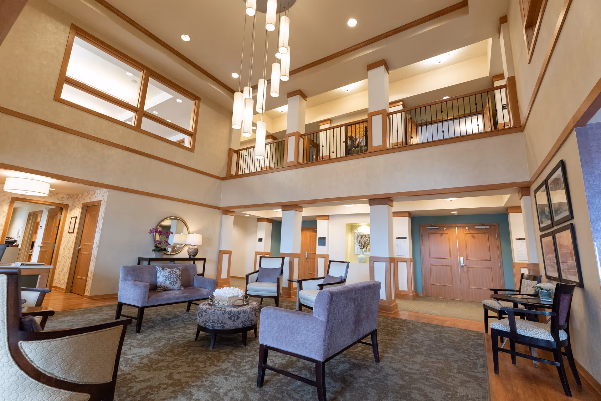 Two-story senior living lobby with seating area, hanging pendant lights, and a second-floor balcony.