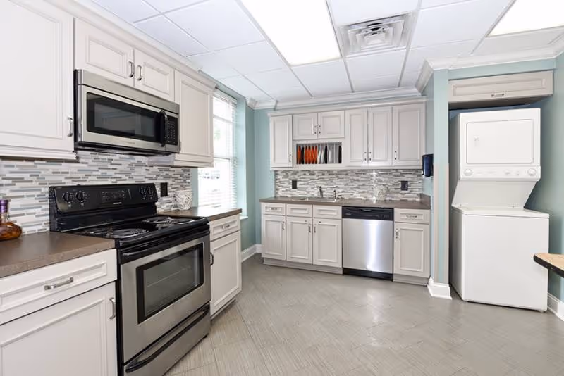 Bright modern kitchen with white cabinets, stainless steel appliances, a tiled backsplash, and a stacked washer-dryer.