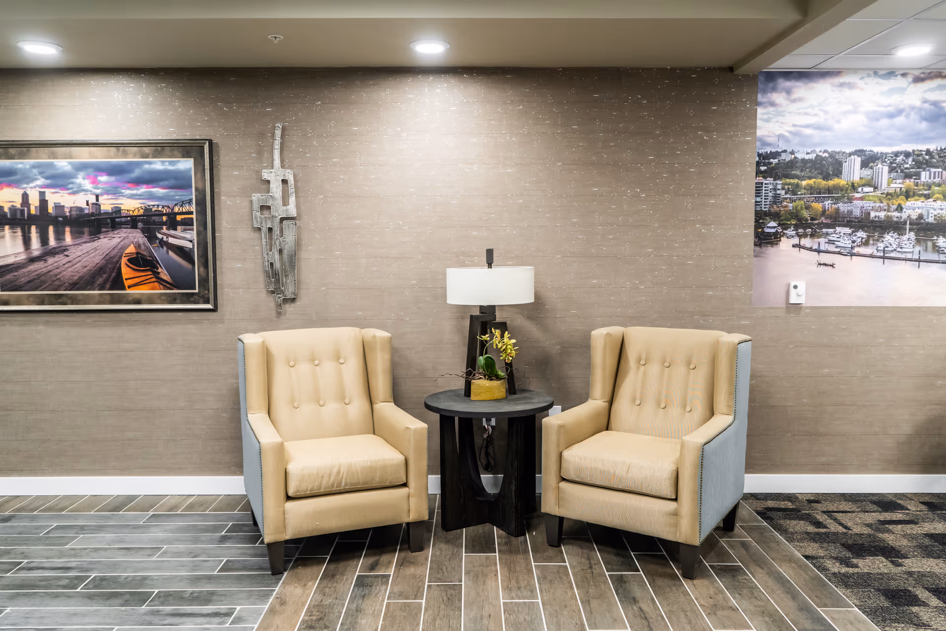 Two beige armchairs flank a small round table with a lamp against a textured wall in a seating area.