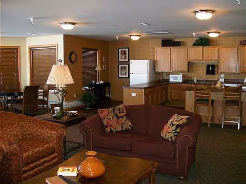 Cozy senior living lounge area with sofas and an open kitchen in the background.