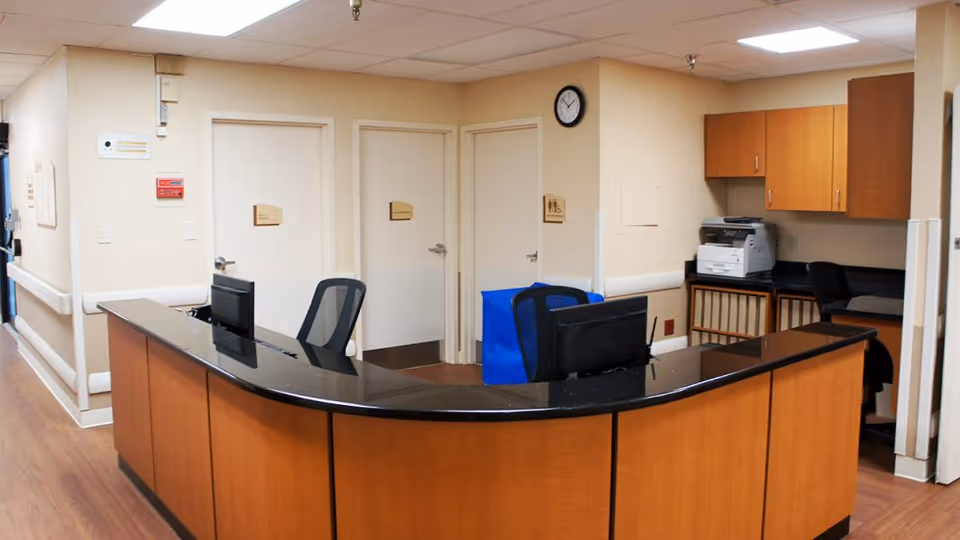 Curved wood nurse/reception desk with computers and chairs in a hallway area of a nursing facility.