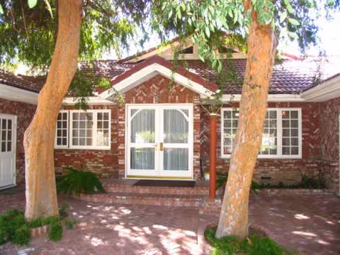 Brick building with a central front door, flanked by two large trees and a shaded walkway.