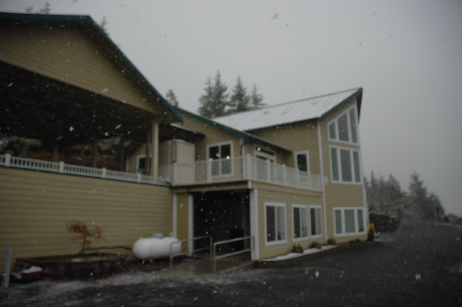 Exterior view of a two-story building with beige siding and large windows, surrounded by trees and light snowfall.
