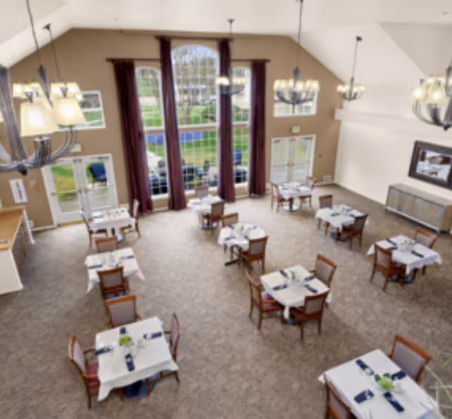 Spacious dining room with multiple set tables, high ceilings, large arched windows, and chandeliers.