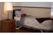 Single adjustable bed in a modest bedroom with patterned bedding, a nightstand and lamp next to a window.