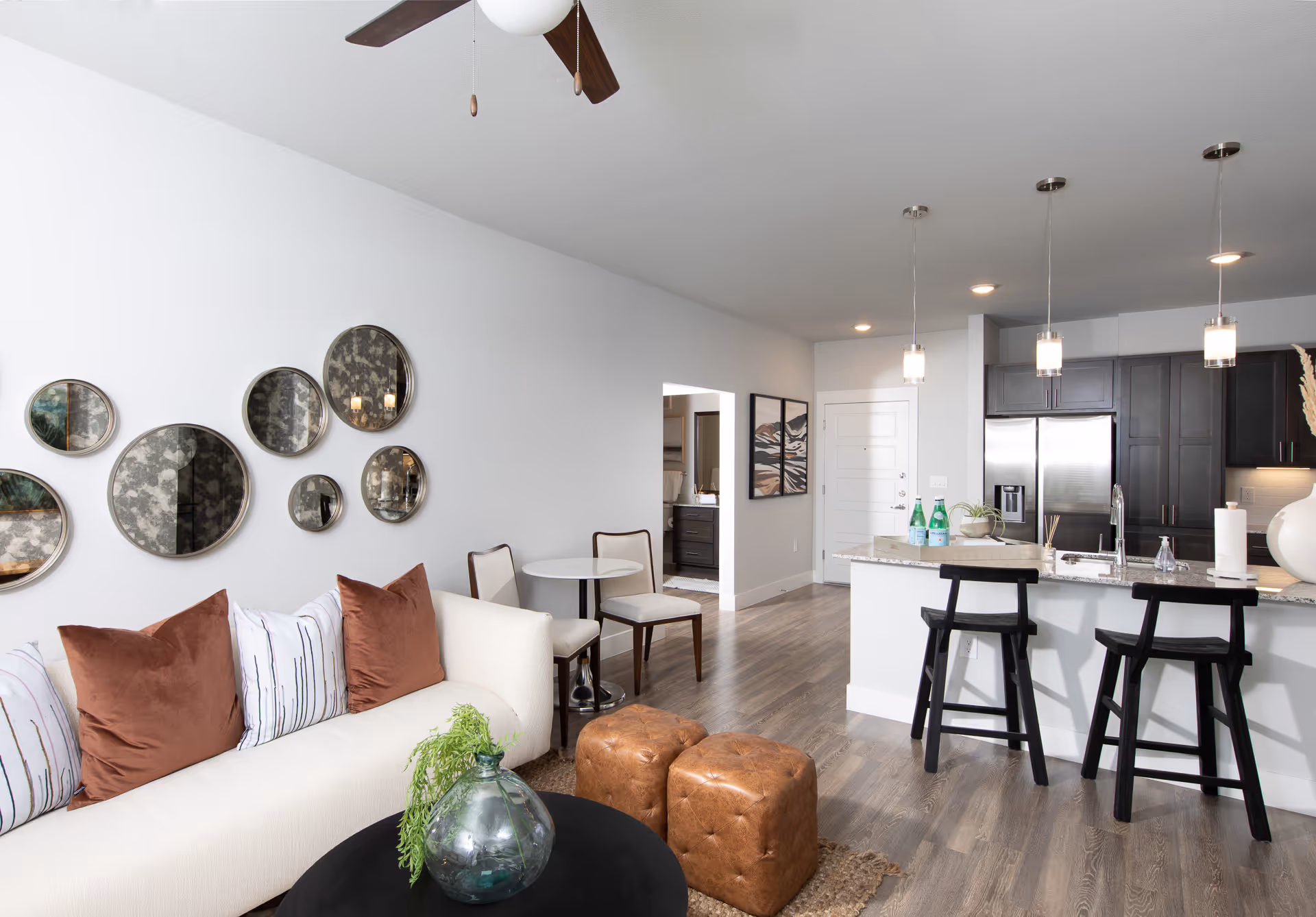 Open-plan living room and kitchen with a white sofa, round wall mirrors, island with bar stools, and pendant lights.