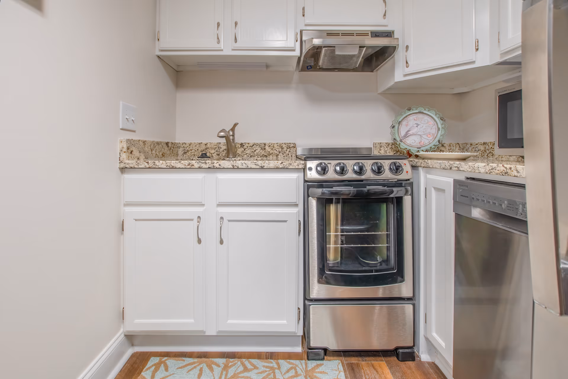 Small kitchen with white cabinets, granite countertops, a stainless steel stove and dishwasher.