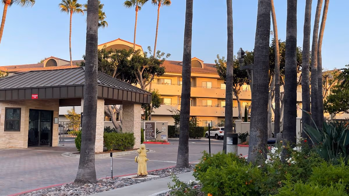 Front entrance and porte-cochere of a multi-story senior living building with palm trees, landscaping, and a fire hydrant.