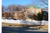 Exterior view of a brick assisted living facility with a white picket fence along the street