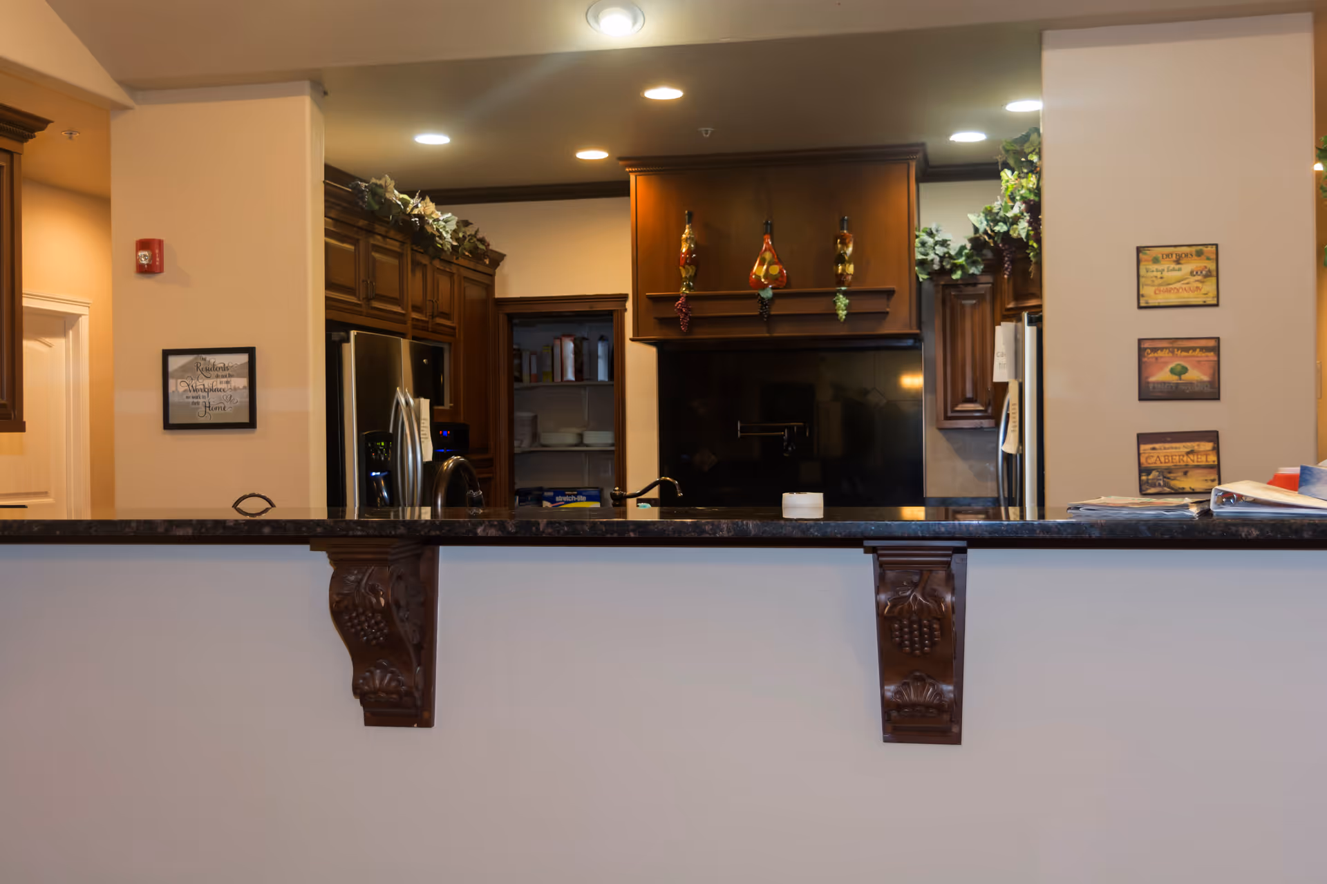 Open kitchen with a dark marble countertop breakfast bar, dark wood cabinetry, stainless refrigerator, and decorative accents.