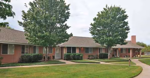 Front exterior of a single-story senior living facility with a lawn, walkway, and trees.