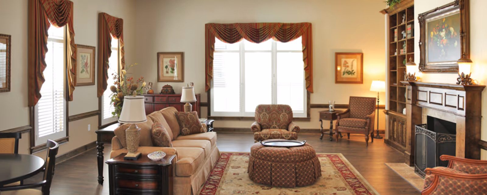 Spacious, traditionally furnished living room with a sofa, armchairs, ottoman, fireplace, and large windows.
