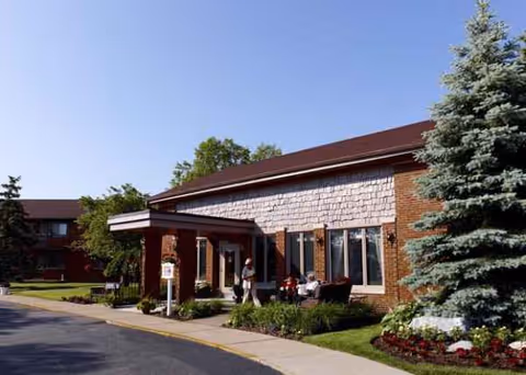 American House East II senior living exterior with brick facade, entrance canopy, and residents seated outside.