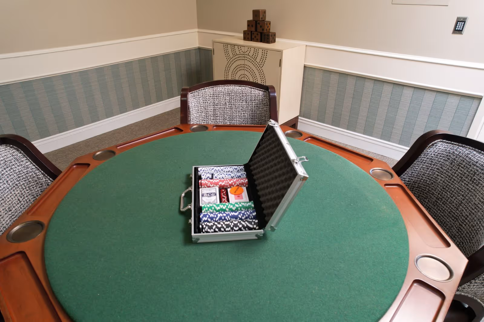 Green felt poker table with an open case of poker chips and surrounding chairs in a small activity room.