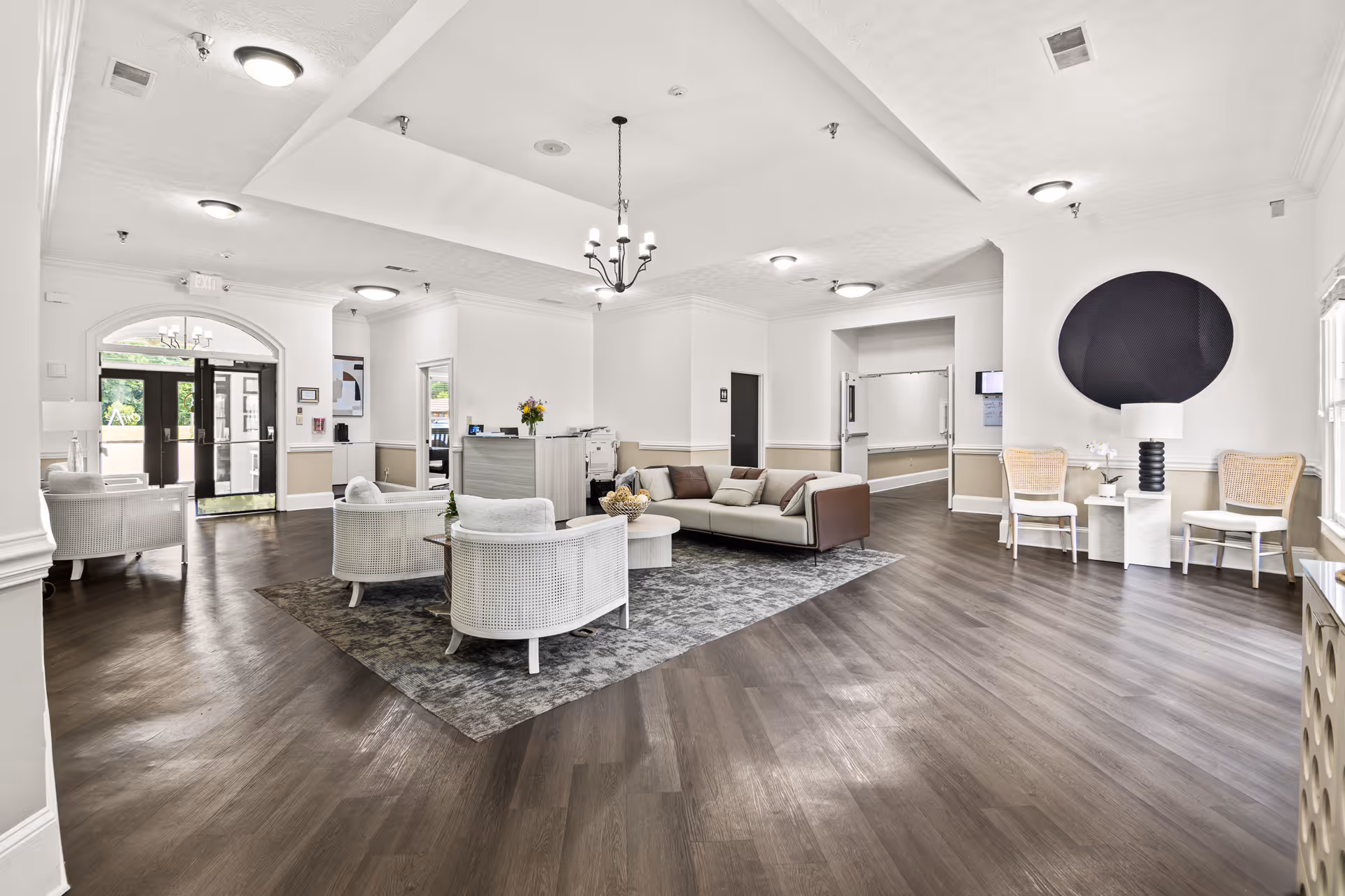 Bright, airy assisted living lobby with a central seating area, reception desk, and wood flooring.