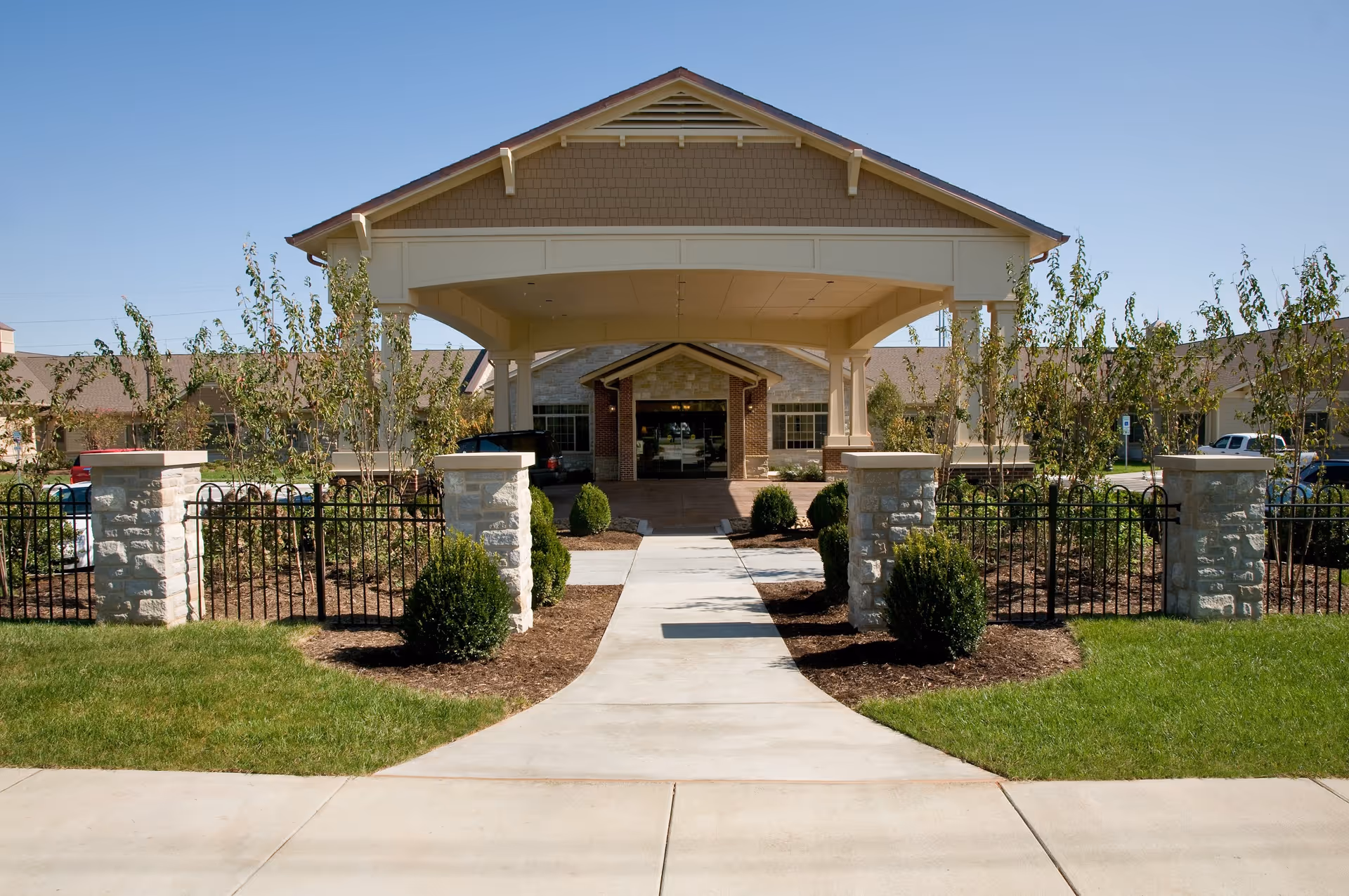 Front entrance of the Life Care Center building with a covered porte-cochère, walkway, landscaping, and stone pillars.