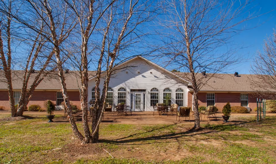 Front exterior of a one‑story brick building with a central white entrance and patio seating framed by leafless trees.