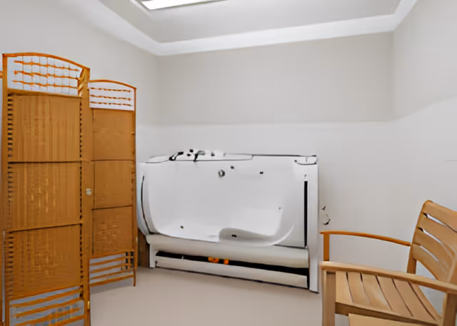 Room with a white walk-in bathtub next to a wooden privacy screen and a wooden chair.