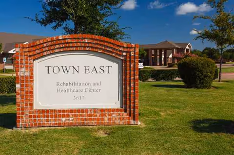 A brick Town East sign sits on a grassy lawn in front of the facility.