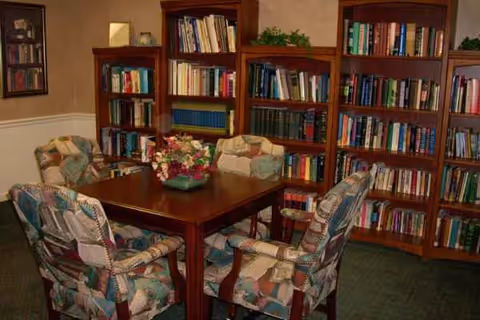 Wood-paneled interior with a central wooden table, cushioned chairs, and tall bookshelves.