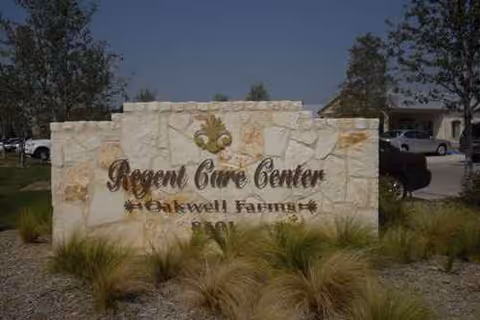 Stone entrance sign reads Regent Care Center Oakwell Farms with ornamental grasses.