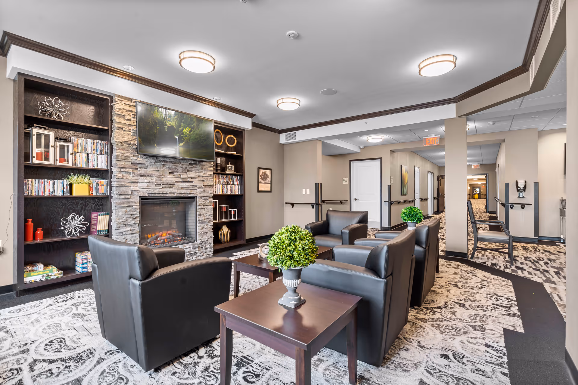 Comfortable lounge with leather chairs around a coffee table facing a stone fireplace and wall-mounted TV with built-in bookshelves.