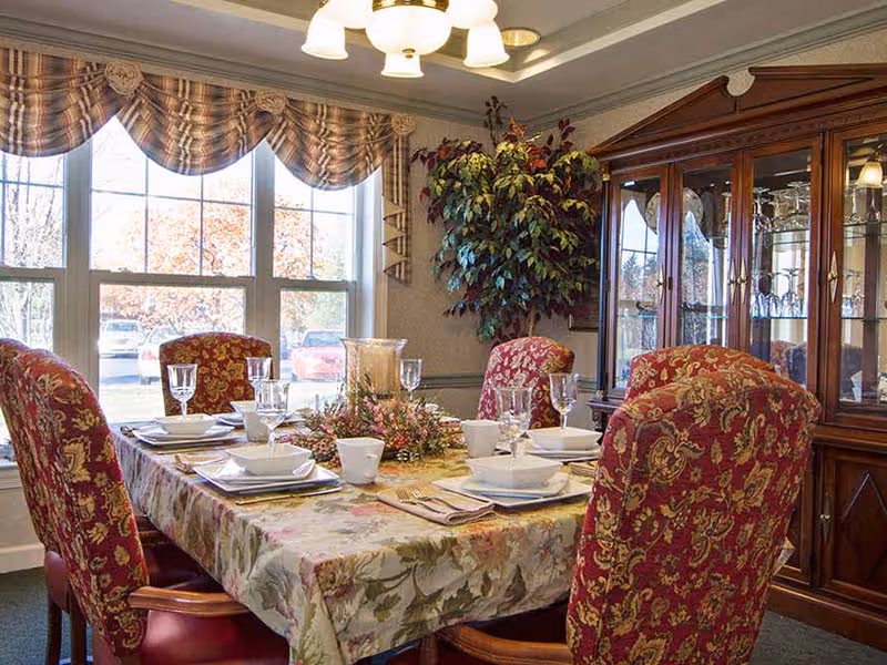 Formal dining room with a set table, patterned upholstered chairs, a china cabinet, and a large window.