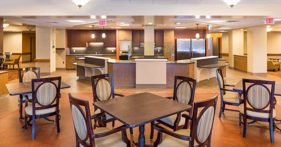 Open communal dining area with several tables and chairs facing a central kitchen and serving counters.