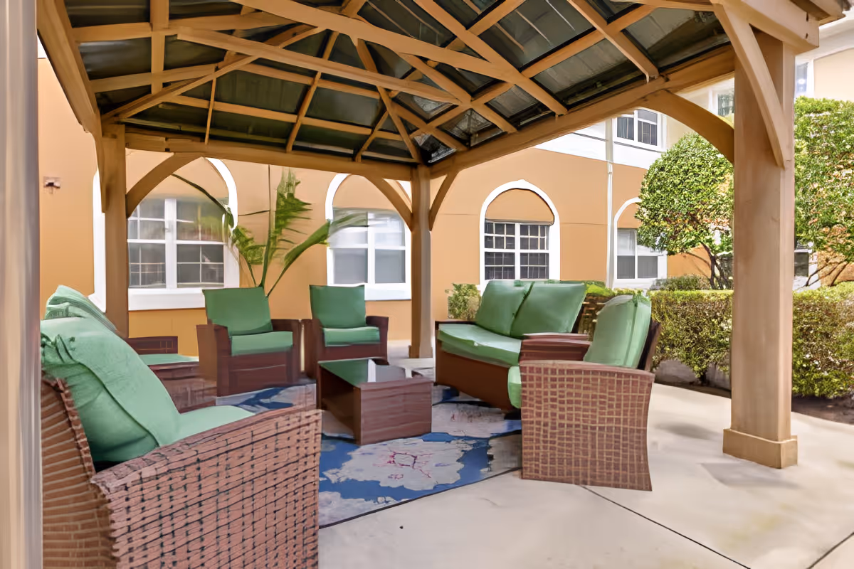 Outdoor courtyard gazebo with green-cushioned wicker chairs, sofas, a rug and a coffee table under a wooden pergola.