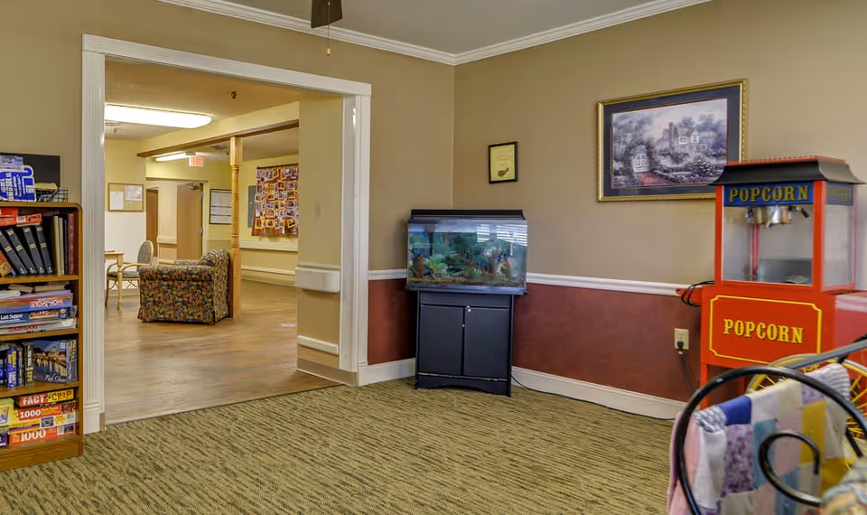 Interior common area showing a popcorn machine, fish tank on a cabinet, bookshelf and a view into a seating area with chairs and a floral couch.