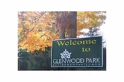 A green welcome sign for Glenwood Park Retirement Village with a tree logo, set outdoors with trees showing autumn foliage in the background.
