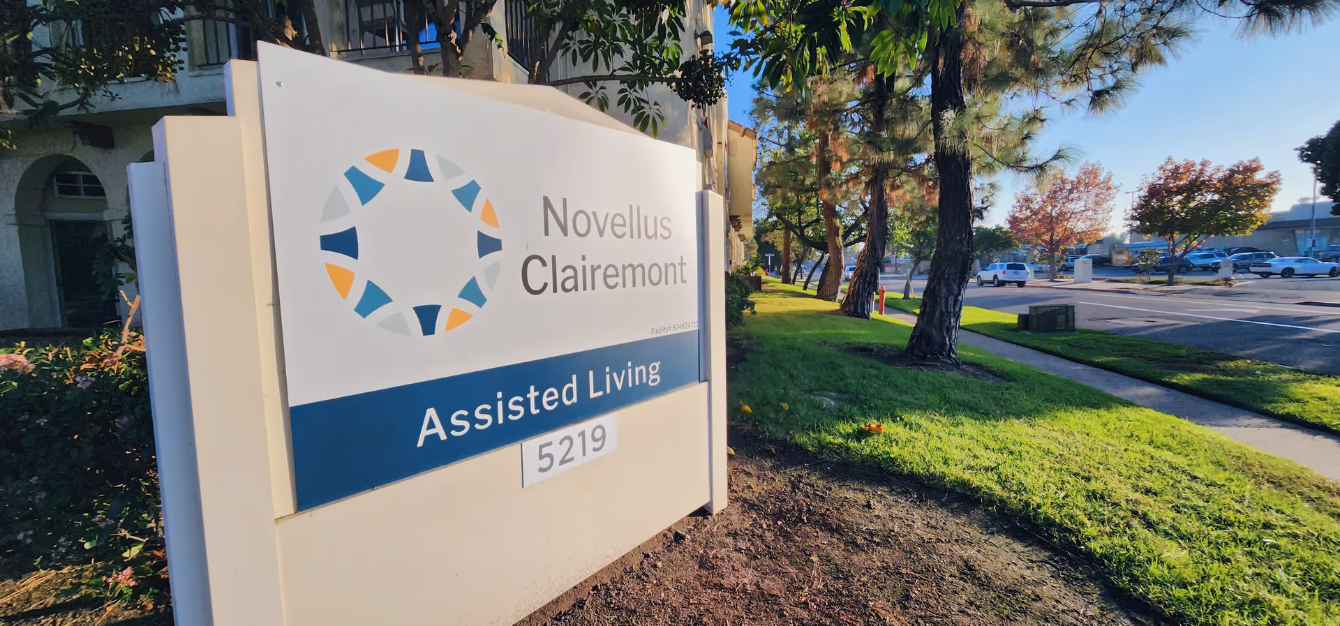 Exterior sign for Novellus Clairemont Assisted Living with landscaping and a parking lot nearby.