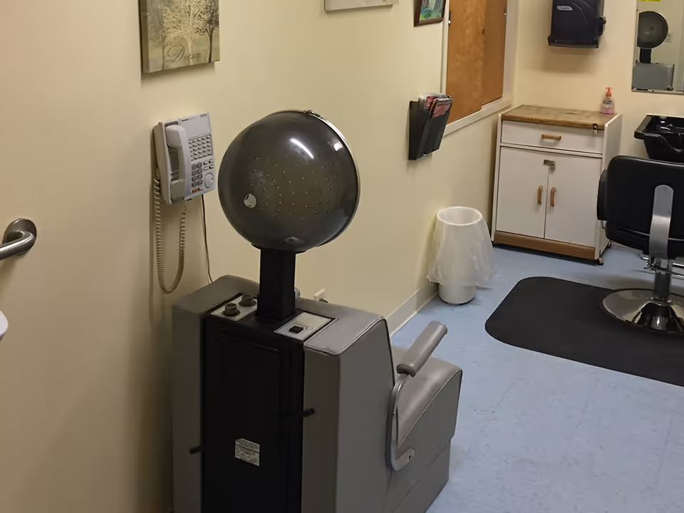 Small salon room with a vintage hooded hair dryer on a chair, a styling chair and sink next to a cabinet.