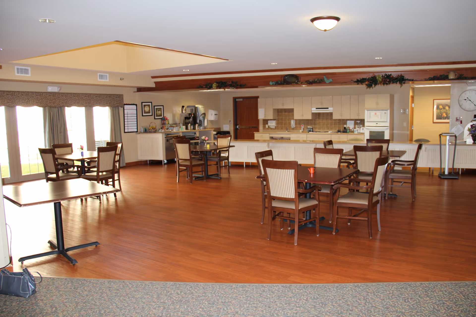 Spacious dining room with wooden tables and chairs and a serving kitchen along the back wall.
