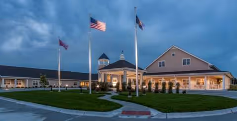 Exterior view of Brookestone Acres with flagpoles, illuminated entrance, and manicured landscaping.