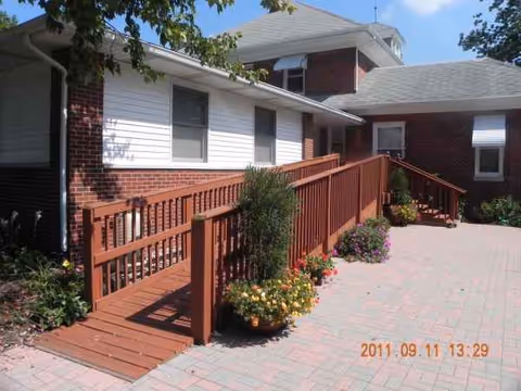 Exterior of a senior living facility featuring brick, white siding, and a wooden ramp.