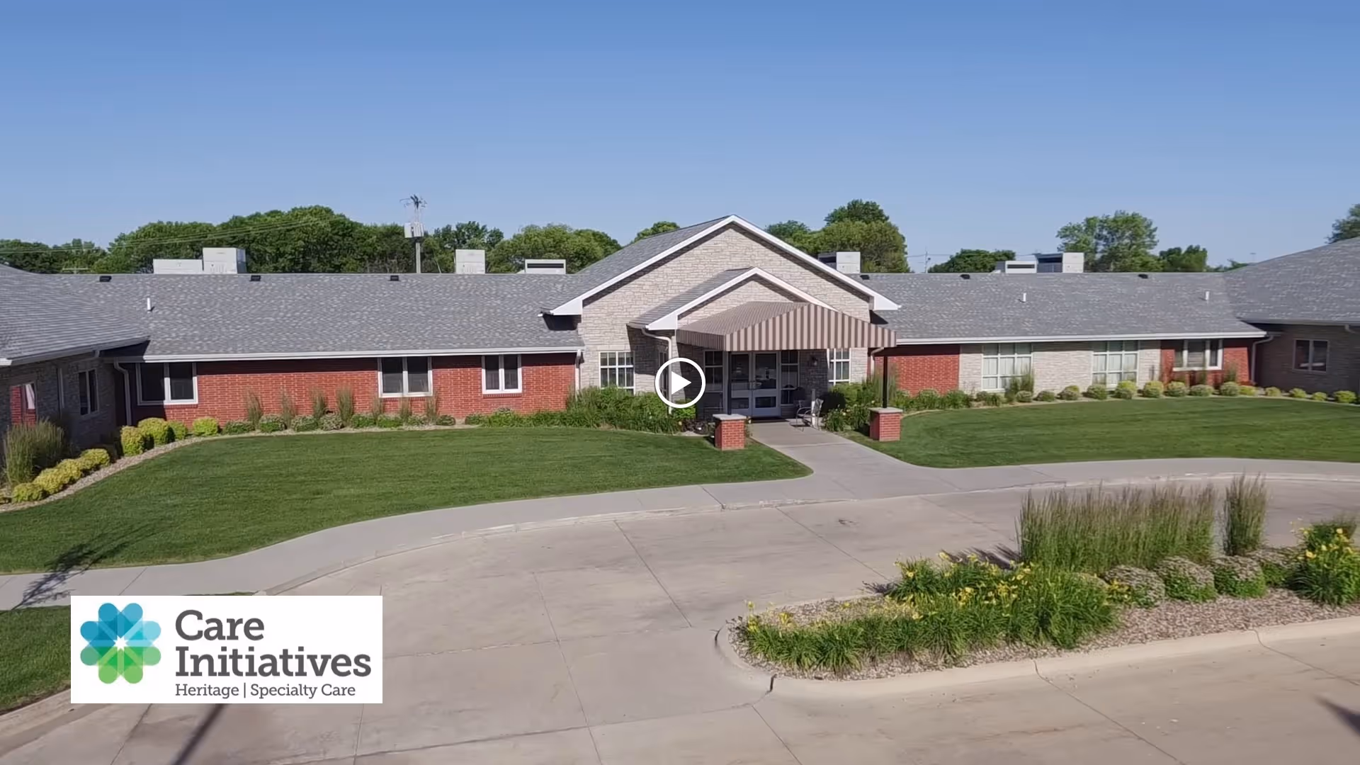 Front exterior of a single-story senior care building with a covered entrance, driveway and landscaped lawn.