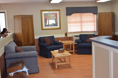 Comfortable common lounge with armchairs, coffee tables, framed artwork, and a reception counter.